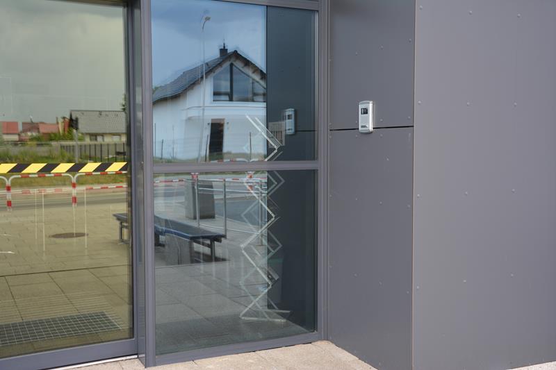 Po prawej stronie drzwi wejściowych do budynku, które otwierają się automatycznie, na ścianie znajduje się domofon.