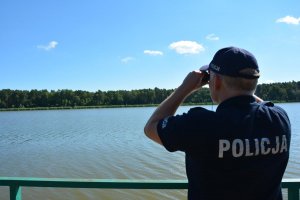 policjant przez lornetkę obserwuje brzeg jeziora