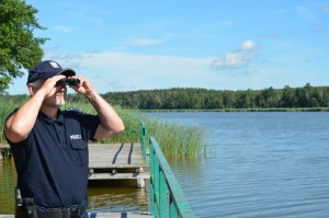 policjant przez lornetkę obserwuje brzeg jeziora
