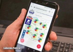 Telefon komórkowy z widoczną mapą Polski w dłoni - w tle klawiatura od komputera