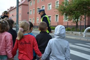 policjant przy przejściu dla pieszych rozmawia z dziećmi