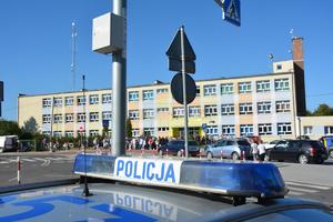 napis policja na radiowozie, w tle droga i osoby przy szkole