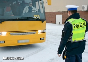 Policjant sprawdza przednie oświetlenie autobusu.