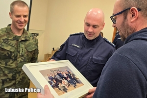 Komendant Powiatowy Policji w obecności żołnierzy wręcza dyrektorowi placówki pamiątkowe zdjęcie