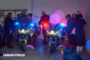 Dzieci w obecności policjanta oglądają motocykle, w których włączone są światła błyskowe.