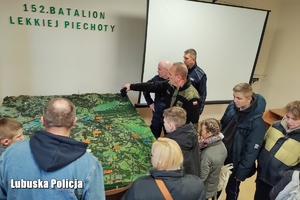 Żołnierz pokazuje dzieciom i opiekunom mapę przekrojową Polski.