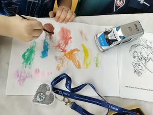 dziecko maluje, na stole leżą kolorowanki i gadżety policyjne