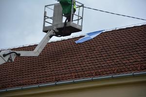 mężczyzna na wysięgniku wiesza na dachu symbol, że obiekt jest zabytkiem