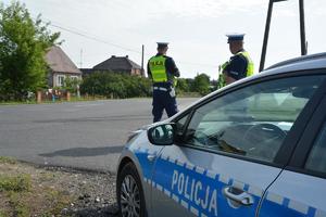 napis policja na radiowozie, w tle policjanci obserwują ruch kołowy