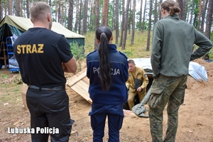 Przedstawiciele Policji i Straży Pożarnej  podczas kontroli obozu. Strażak wychodzi z ziemianki.