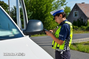 Policjantka stojąc przy pojeździe sprawdza w systemach policyjnych dane kierującego i samochodu