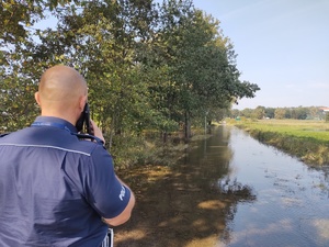 policjant rozmawia przez telefon przy zalanej drodze