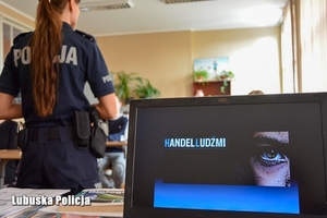 ekran monitora z napisem Handel Ludźmi, w tle policjantka prowadzi spotkanie z młodzieżą