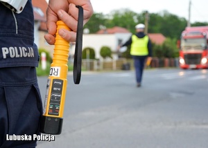 urządzenie do kontroli stanu trzeźwości w rękach policjanta, w tle policyjne kontrole