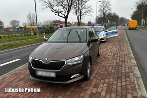 samochód stojący na powierzchni wyłączonej z ruchu, a za nim radiowóz