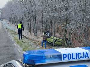 napis policja na dachu radiowozu, w tle pojazd leżący w rowie na dachu, obok policjanci