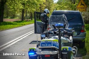 policyjny motocykl za samochodem przy którym stoi policjant