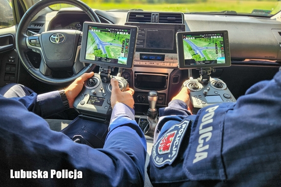 policjanci siedząc w samochodzie trzymają w rękach urządzenie do obsługi drona