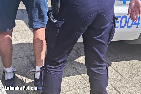 policjant prowadzi mężczyznę, który ma kajdanki założone na nogi