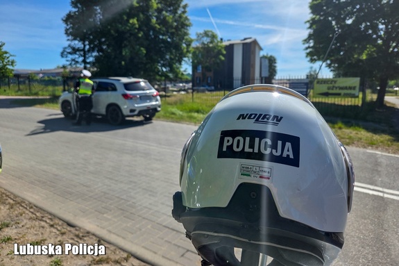 kask motocyklowy z napisem policja, w tle policjant kontroluje kierowcę samochodu